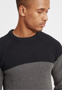 Pulover tricotat cu guler rotund, secțiune superioară de culoare bleumarin închis, și o bandă de mijloc texturată de culoare gri deschis. Material neted cu un model fin.