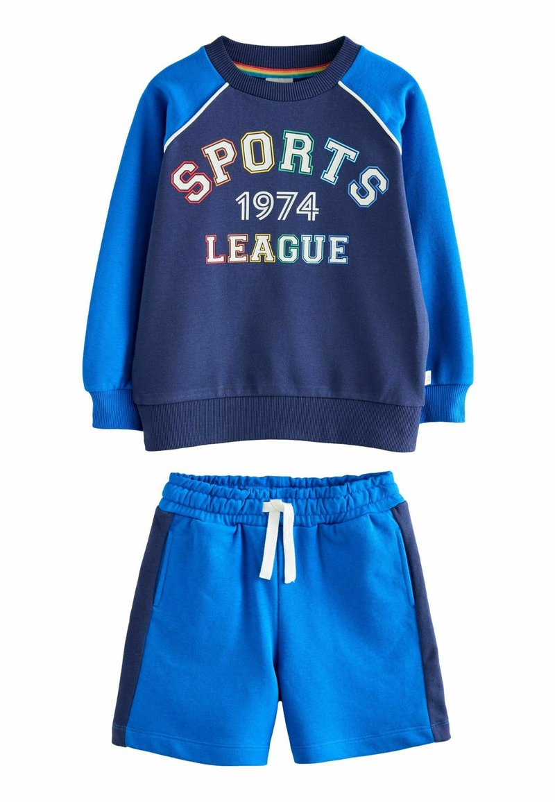 Námornícky modrý sveter s nápisom "SPORTS LEAGUE 1974" v farebnom texte, skombinovaný s modrými šortkami s elastickým pásom a vreckami.