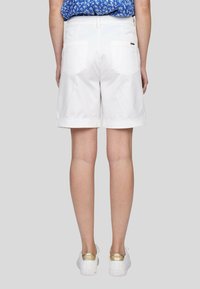 Shorts en coton blancs avec des ourlets roulés, deux poches arrière et une petite étiquette de logo. Assortis à des chaussures blanches avec des accents dorés.