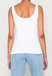Camiseta sin mangas blanca con un diseño de espalda en forma de scoop, hecha de una tela suave, con tirantes finos y un corte clásico. Combinada con jeans de color azul claro.