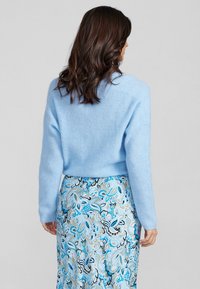 Hellblauer gestrickter Pullover mit einer lockeren Passform, der über eine gerippte Textur und lange Ärmel verfügt, kombiniert mit einem gemusterten blau-weißen Rock.