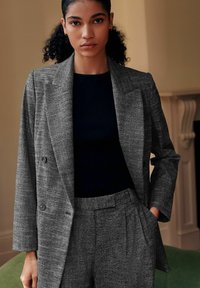 Grijze getextureerde double-breasted blazer met scherpe revers en lichte padding, gecombineerd met een aansluitend zwart ribbeltop en bijpassende broek.