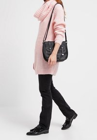 Pull en tricot rose clair avec un col bénitier, associé à un pantalon noir et des chaussures noires brillantes. Sac à bandoulière noir avec des accents en argent.