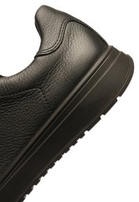 Black leather sneaker with textured upper, rounded toe, and contrasting rubber sole featuring a tread pattern for grip.