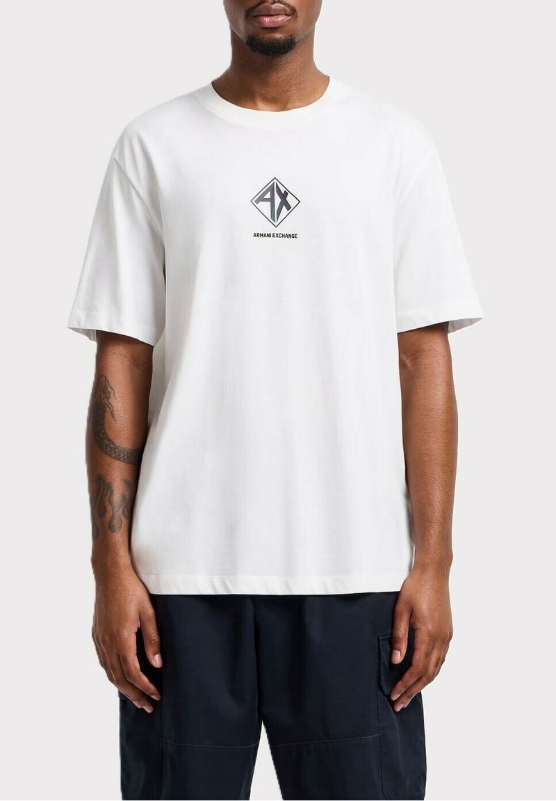 T-shirt bianco a maniche corte in cotone con vestibilità ampia. Caratterizzato da un logo centrale nero a forma di diamante con il testo "AX" e "ARMANI EXCHANGE" sottostante.