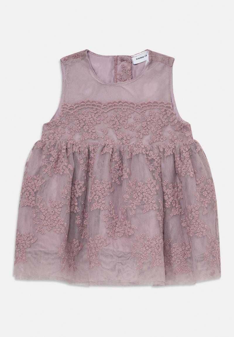 Vestido rosa com design sem mangas, apresentando sobreposição de renda floral, saia em camadas e fechamento por botão nas costas. Tecido macio e texturizado.