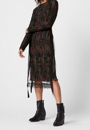 Femme portant une robe midi noire avec des motifs cachemire colorés, une bordure en dentelle et des bottines noires avec des fermetures éclair.