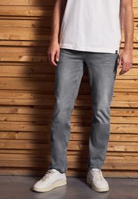 Vaqueros de mezclilla gris con un corte ajustado, que presentan una textura suave. Combinados con zapatillas blancas frente a un fondo de madera.