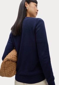 Marineblauer Strickpullover mit Rundhalsausschnitt und gerippten Bündchen, kombiniert mit einer strukturierten, beigefarbenen Baumwolltasche. Einfaches, klassisches Design.
