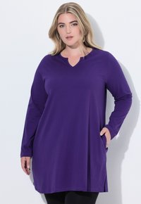 Fioletowa tunika z długim rękawem, w serek i z kieszeniami po bokach, wykonana z miękkiego materiału, z luźnym krojem i gładką fakturą.