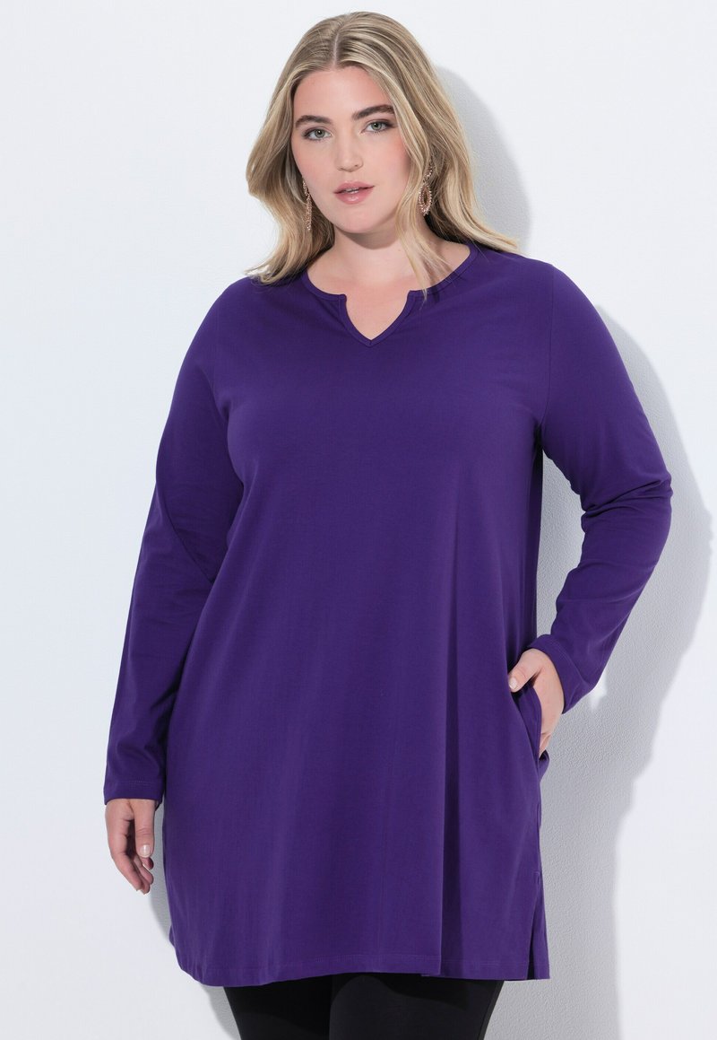 Fioletowa tunika z długim rękawem, w serek i z kieszeniami po bokach, wykonana z miękkiego materiału, z luźnym krojem i gładką fakturą.