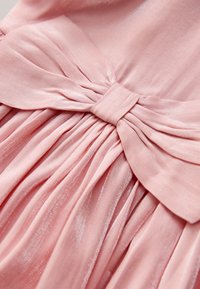 Tela rosa suave recogida en un lazo estructurado con pliegues plisados, mostrando una textura suave y detalles elegantes de drapeado.
