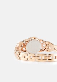 Roséguld klocka med länkarmband, som har ett slätt boett och en rund, minimalistisk urtavla. Varumärket "Guess" är graverat.