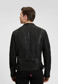 Zwarte leren motorjack met een rechte snit, textuurpanelen op de schouders en twee zijritsen voor verstelbaarheid.