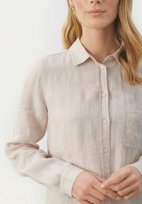 Lysebrun hørskjorte med krave, knaplukning foran, enkelt brystlomme og lange ærmer. Blød tekstur og afslappet design.