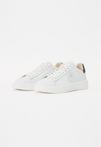 Adidași albi din piele netedă, cu vârf rotunjit, șireturi în față și logo embosat pe lateral. Prezintă un tab din material închis la culoare pe călcâi.