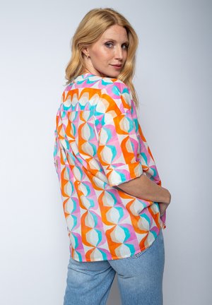 Bunt gemustertes kurzärmeliges Hemd mit einem geometrischen Muster in Orange, Pink und Türkis auf hellen Hintergrund, aus leichtem Stoff gefertigt.