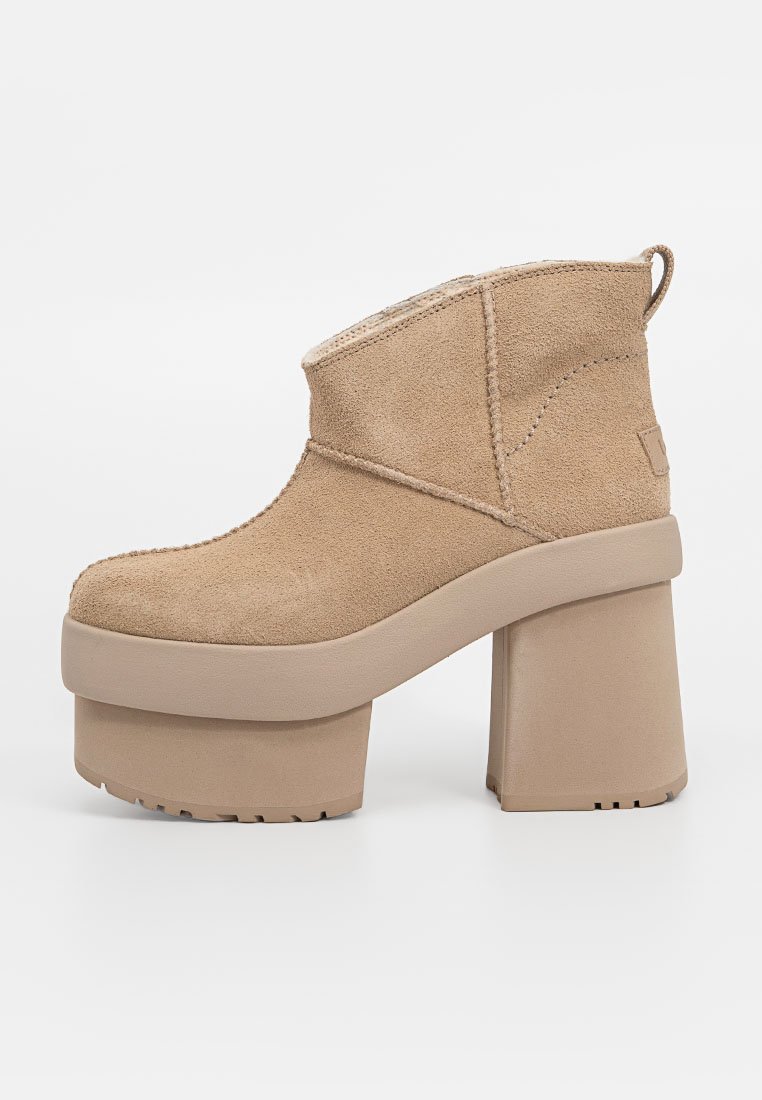 Botines de ante beige con punta redondeada, plataforma alta y tacón de bloque grueso. Presentan un diseño de costura y una pestaña en la parte posterior.