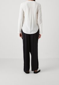 Vit långärmad blus med veck bak, rundad nederkant, ihopparad med svarta vida byxor. Slät tyg, enkel design, inga mönster.