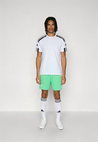 White athletic t-shirt with black stripes on sleeves, paired with green shorts. Accessories include white socks with black stripes and cleats.