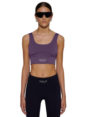 Kvinde iført lilla crop top og sorte leggings med "HALO"-logo, store sorte solbriller og sølv hoop-øreringe, står vendt fremad.
