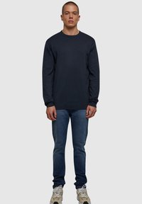 Marineblå langermet skjorte i bomull, rund hals, avslappet passform, kombinert med blå slim jeans og lyse sneakers.