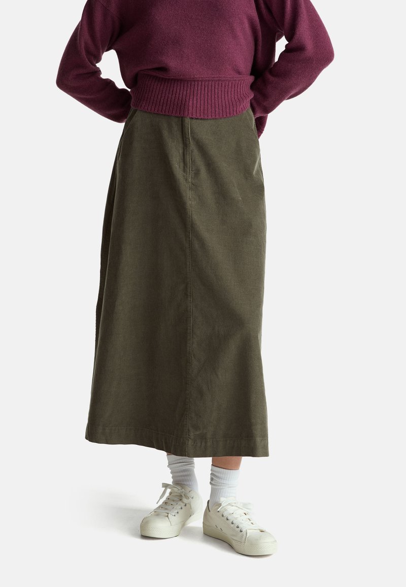 Olivově zelená kordurová maxi sukně s proužkovaným pasem, v kombinaci s bílými teniskami a pruhovanými ponožkami. Měkká textura, rovný střih.