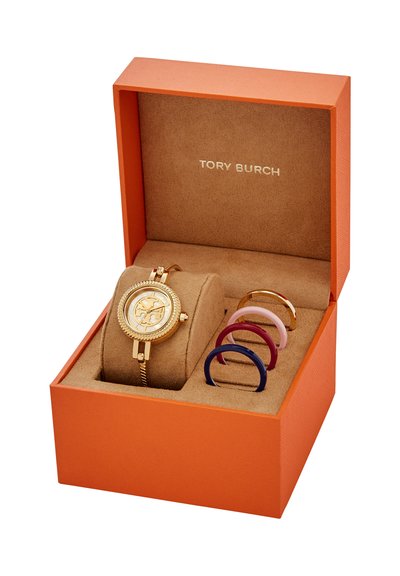 Guldfärgad Tory Burch-klocka med utbytbara färgglada ramar i en öppen orange ask med beige insida.