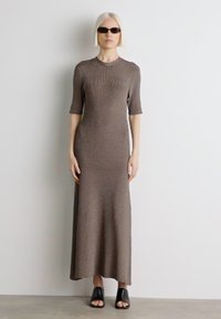 Piklik, pruun soonikko dress koos lühikeste varrukatega ja ümarate kaelustega, millele on sobitatud mustad avatud varvastega sussid ja peened tumedad prillid.