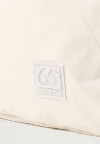 Crème-kleurige stof met een gladde textuur heeft een prominent wit vierkant logo-detail met daarop "66° NORTH" in vette letters.