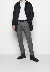 Manteau noir à col, doublé de fausse fourrure, col roulé blanc, pantalon gris ajusté et bottines noires à semelles épaisses.