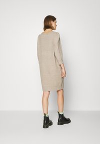 Abito in maglia beige con vestibilità comoda, maniche a tre quarti e scollatura a barca. Indossato con stivali neri con dettagli verdi alla caviglia.