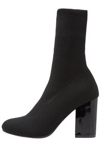 Botte de cheville noire en forme de chaussette avec une texture côtelée, un dessus ajusté et un talon carré noir brillant. Design élégant et moderne.
