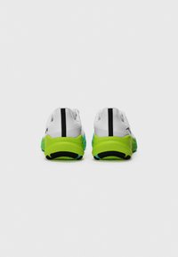 Des chaussures de sport blanches avec une semelle verte et bleue, présentant une bande noire à l'arrière et un tissu texturé pour une meilleure adhérence et un soutien optimal.