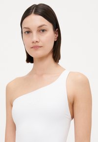 Maillot de bain blanc à une épaule en tissu lisse, présentant un détail logo subtil. Le design est minimaliste et ajusté.