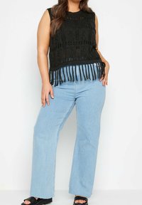 Czarny top na ramiączkach z szydełkowym wykończeniem z frędzlami, w połączeniu z jasnoniebieskimi spodniami typu wide-leg i czarnymi sandałami na platformie.
