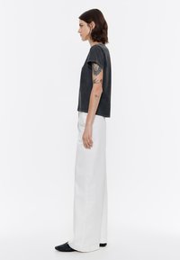 Camiseta de algodón gris, de mangas cortas y cuello redondo. Combinada con pantalones de pierna ancha blancos de cintura alta y calzado negro.