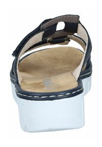 Mörkblå lädersandal med justerbar rem, platt vit sula och beige vadderad innersula. Har stickningsdetaljer längs kanten.