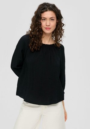 Zwarte blouse met lange mouwen van textuurstof, met een geplooide halslijn en een relaxte pasvorm, gecombineerd met lichtgekleurde broek. Geen zichtbare patronen of accenten.