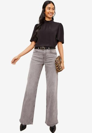 Blouse noire à volants associée à un jean gris taille haute et à jambes larges. Accentué par une ceinture noire et une pochette à imprimé léopard. Escarpins noirs à talons pointus.
