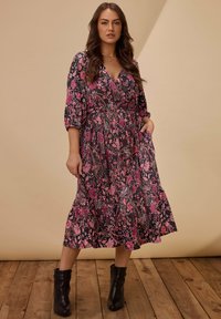 Floral wrap dress in black with pink patterns; three-quarter sleeves; knee-length; features a flared hem; styled with black ankle boots.