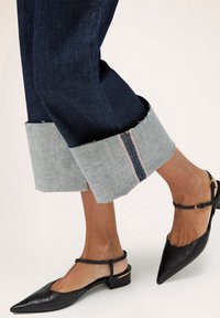 Blugi din denim cu manșete ușor răsucite de culoare albastră deschisă, accentuate cu o cusătură roșie contrastantă; asortați cu balerini negri cu vârf ascuțit și toc mic.