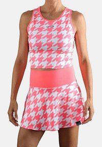 Mujer vestida con un top corto sin mangas de un estampado de pata de gallo en rosa y blanco, acompañado de una falda de tenis de talle alto a juego.