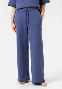 Blauwe, wijde sweatpants van zacht materiaal, met een elastische tailleband met koord en zijzakken. Kleine tekstdetails aan de voorkant.