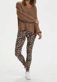 Brun stickad tröja med v-ringning och långa ärmar, kombinerad med figurnära leggings med leopardtryck och vita sneakers.