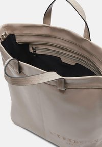 Sac fourre-tout en cuir beige avec une texture lisse. Dispose de deux poignées, d'une poche zippée à l'intérieur et d'un logo en relief à l'extérieur.