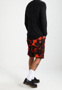 Szorty typu cargo w pomarańczowo-czarny wzór moro, zestawione z czarną koszulą na długi rękaw, białymi skarpetkami i czarnymi butami na sznurówki.