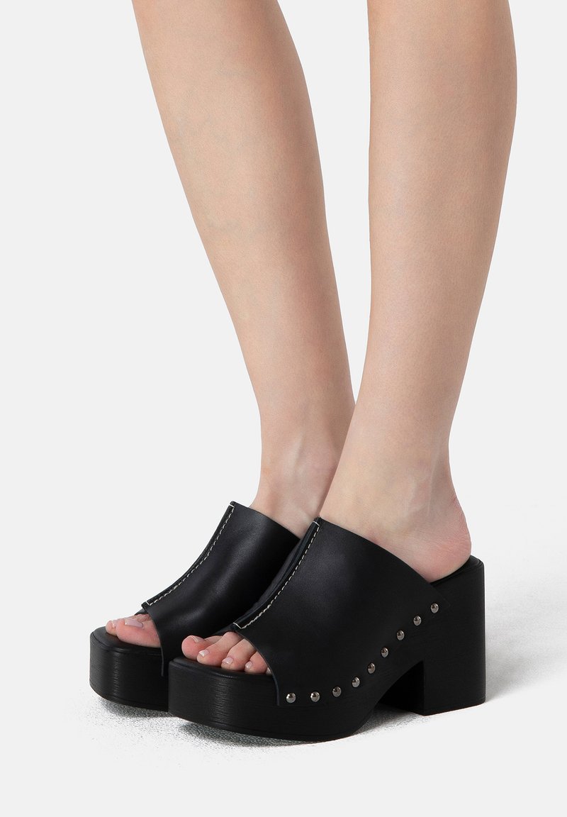 Black platform mules made of smooth leather, featuring an open toe, side cutouts, and silver stud detailing along the outer edge.