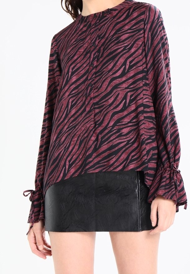 Blouse à motifs zèbre dans des tons marron et noir, avec des manches longues et des détails à nouer aux poignets, assortie à une mini jupe noire texturée.