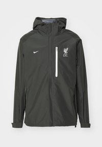 Mørkegrøn vandtæt jakke med hætte, der har en hvid lynlåslomme på brystet, Nike-logo og Liverpool FC-emblem på venstre bryst.